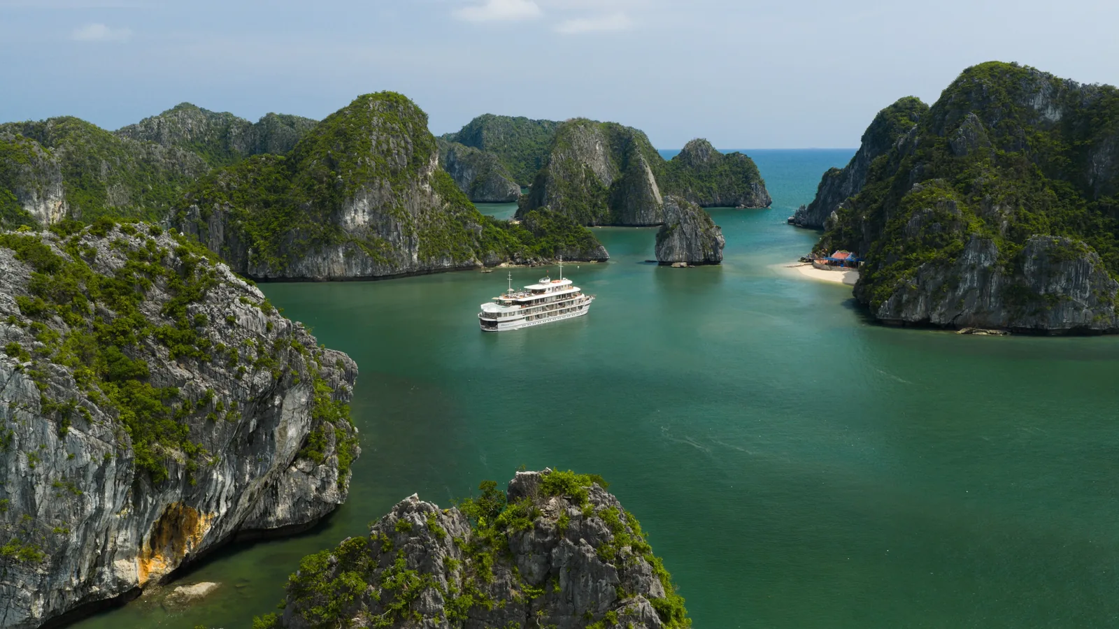 A cruise ship sails through emerald waters surrounded by limestone karsts in Halong Bay, Vietnam.