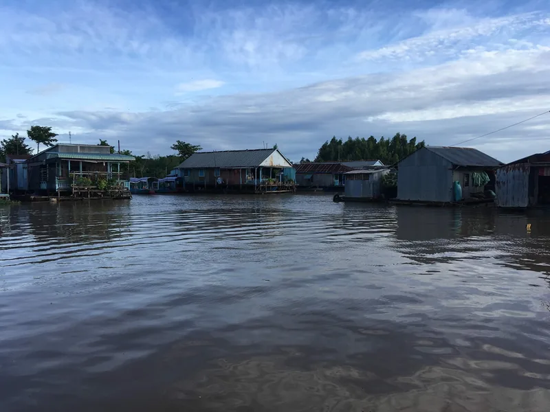 Floating houses line the calm river at a village in Chau Doc under a wide sky.