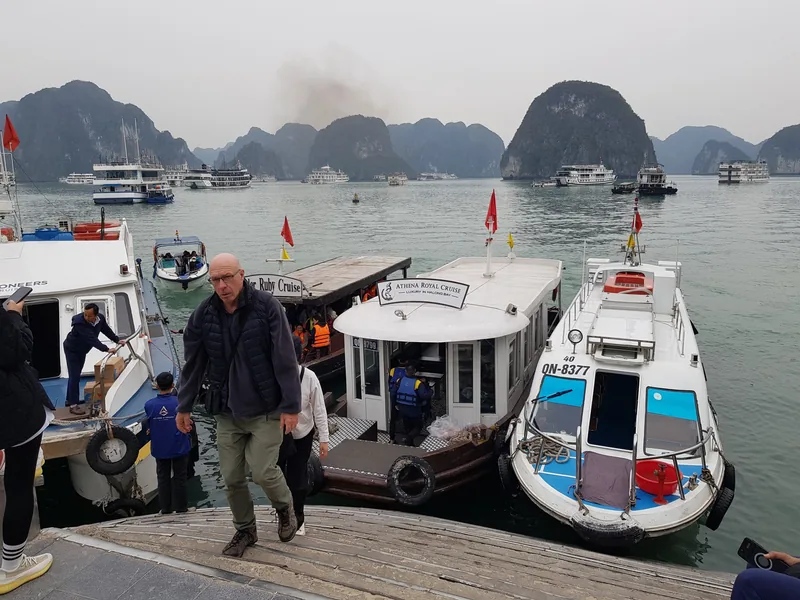 Tourists disembark from tender boats onto a floating pier amid limestone karsts in Halong Bay.