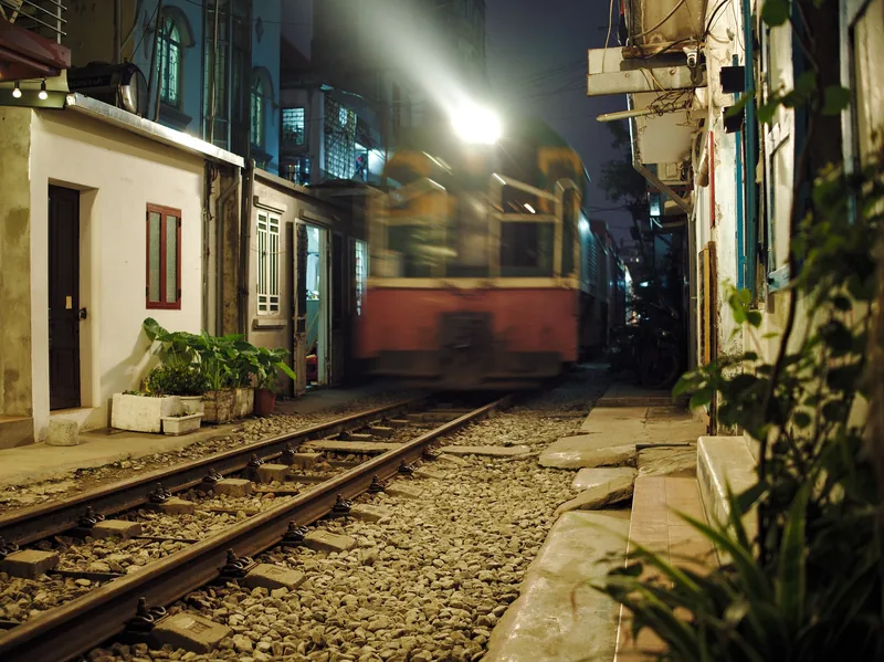 A train passes at night through Hanoi's narrow Train Street, lined with houses close to the tracks.