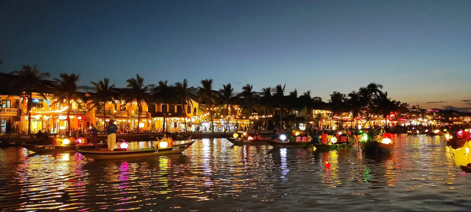 Colorful lantern boats glow on the Thu Bon River at dusk in Hoi An's old town.
