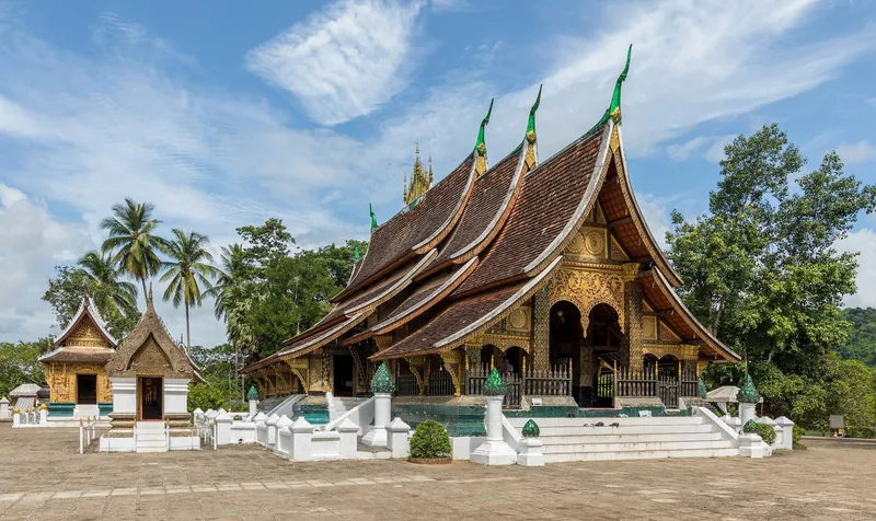Sweeping tiered roofs and golden facade of Wat Xieng Thong temple in Luang Prabang under a bright sky