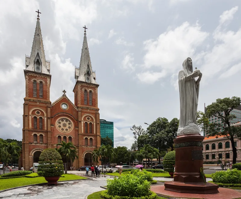 Twin red-brick towers of Notre Dame Cathedral rise beside the Virgin Mary statue in Ho Chi Minh City.
