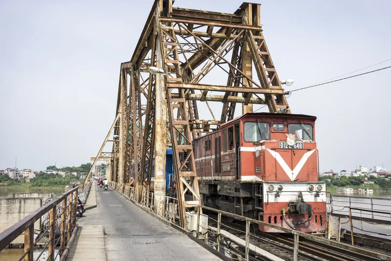 A red locomotive crosses the steel trusses of Long Bien Bridge in Hanoi.